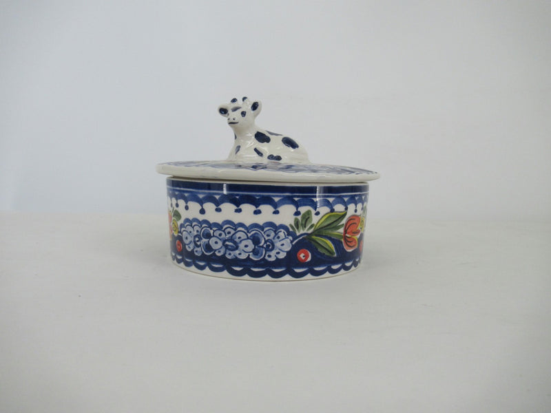 Ceramic round butterdish with a cowshaped lid, painted in delftblue and red tulip.