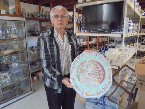 Delftpainter vanderBerg showing his just finished Mucha women on a ceramic plaque.