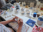 Delftblue painter at a table full of ceramics bisque teapots she is working on