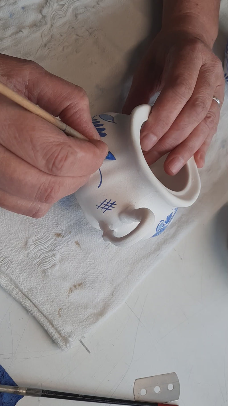 Delftpainter in the process of handpainting a delftblue creamer and sugar set.
